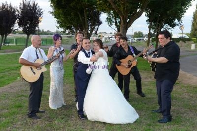 Un couple de mariés dansant entouré de musiciens jouant de la guitare dans un parc verdoyant.
