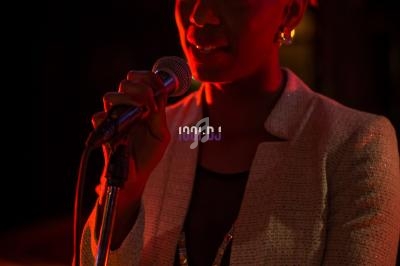 Femme tenant un micro et chantant sur une scène éclairée par des lumières rouges et sombres.