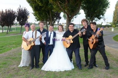 Un groupe de musiciens avec des guitares pose avec un couple de mariés dans un parc verdoyant.