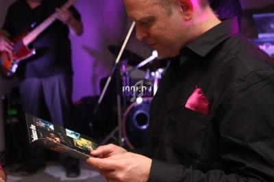 Un homme en chemise noire lit un dépliant lors d'un événement avec des instruments de musique en arrière-plan.