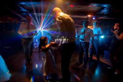 Un homme danse avec une petite fille dans une salle sombre éclairée par des lumières colorées.