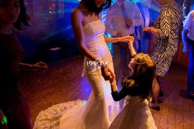 Une femme en robe de mariée danse avec une petite fille sur une piste éclairée par des lumières colorées.