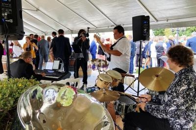 Un groupe de musiciens joue sous une tente lors d'un événement en plein air avec des invités en arrière-plan.