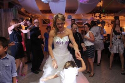 Une mariée danse avec une petite fille au milieu d'invités lors d'une fête dans une salle décorée.