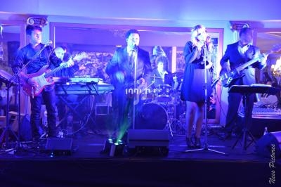 Groupe de musiciens et chanteurs se produisant sur une scène éclairée dans une ambiance festive.