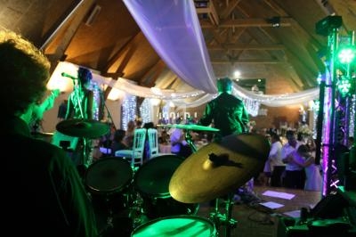 Un groupe de musiciens joue sur scène dans une salle éclairée, avec des invités dansant en arrière-plan.