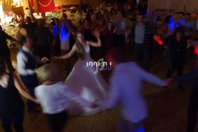 Des invités dansent en cercle autour d'une mariée sur une piste éclairée lors d'une réception de mariage.