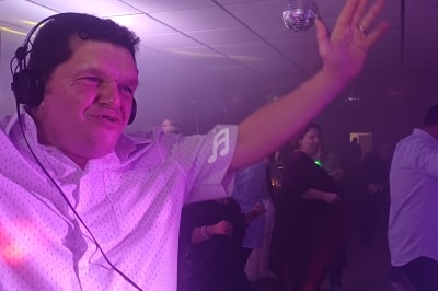 Homme portant un casque audio, bras levés, animant une soirée dansante sous des lumières colorées.