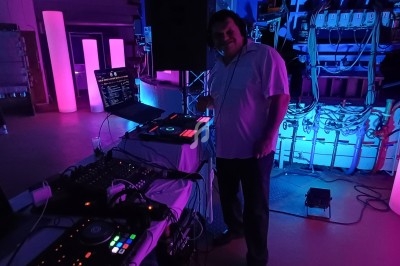 Un DJ mixant de la musique sur une console dans une salle éclairée par des lumières violettes et bleues.