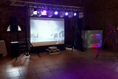 Installation de matériel audiovisuel dans une salle en pierre, avec écran de projection et éclairages colorés.
