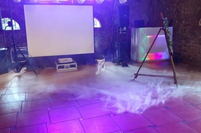 Salle avec écran de projection, éclairages colorés, sol en carrelage et légère fumée au sol.