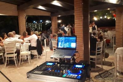 Table de mixage et ordinateur portable installés sous une pergola, avec des invités assis à des tables en arrière-plan.