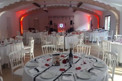 Salle de réception décorée avec des tables rondes dressées, chaises blanches et éclairage rouge en arrière-plan.