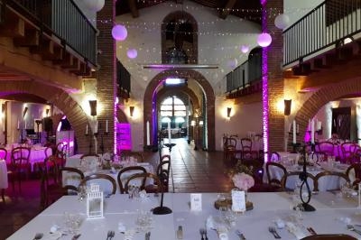 Salle de réception décorée pour un événement, avec tables dressées, chaises en bois et éclairage tamisé violet.