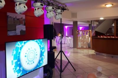 Salle décorée pour un événement avec éclairages colorés, écran affichant une animation et ballons au sol.