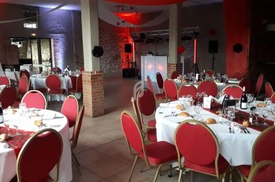 Salle de réception décorée avec des tables rondes dressées, chaises rouges et éclairage tamisé rouge.