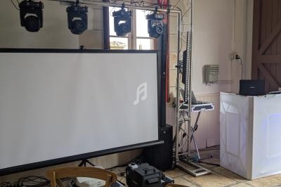 Équipement audiovisuel installé dans une salle avec écran, projecteurs, table de mixage et décor sobre.
