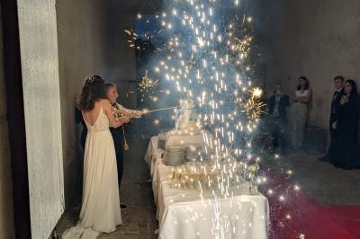 Un couple coupe un gâteau de mariage devant une table décorée, entouré d'étincelles et d'invités.