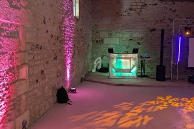Salle en pierre avec éclairage coloré, un pupitre lumineux et des équipements audio installés.