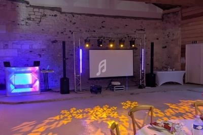 Salle de réception avec éclairage coloré, piste de danse, table dressée et équipement audio-visuel installé.