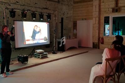 Un photographe projette une image sur un écran dans une salle en pierre, face à une femme assise en robe blanche.
