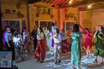 Personnes dansant dans une salle éclairée par des lumières colorées, avec un DJ en arrière-plan.