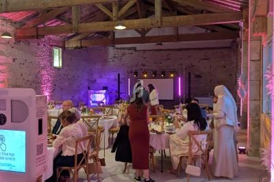 Salle en pierre avec charpente apparente, décorée pour un événement, des invités assis autour de tables éclairées.