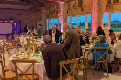 Des invités discutent et dînent dans une salle en bois avec des tables décorées et un éclairage chaleureux.