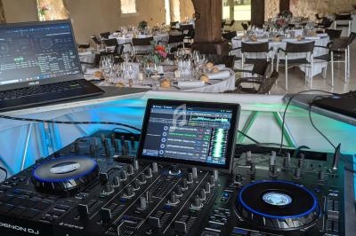 Console de mixage DJ avec ordinateurs dans une salle de réception décorée pour un événement avec tables dressées.