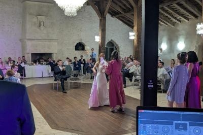 Un couple danse au centre d'une salle de réception avec des invités assis autour, sous un grand lustre.