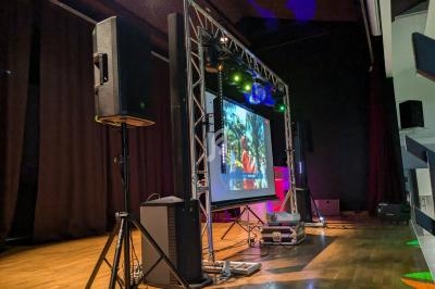 Installation audiovisuelle sur une scène avec écran de projection, projecteurs colorés et haut-parleurs.