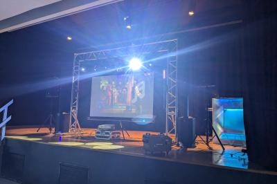 Scène équipée d'un écran géant diffusant une vidéo, entourée de projecteurs et d'équipements audiovisuels.