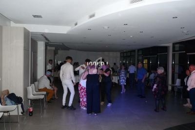 Personnes discutant et dansant dans une salle éclairée, avec des chaises alignées le long des murs.