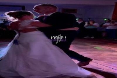 Un couple danse lors d'une soirée, éclairé par des lumières colorées, entouré de spectateurs.