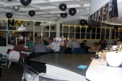 Personnes assises et debout dans une salle décorée de ballons noirs et de guirlandes pour une fête.