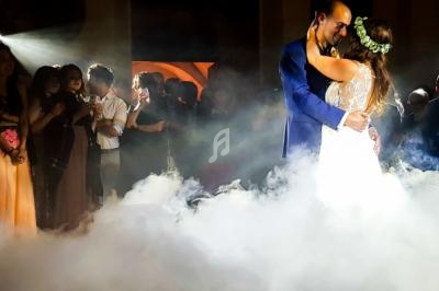 Un couple danse dans une ambiance romantique avec des invités en arrière-plan et un éclairage tamisé.