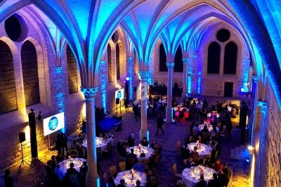 Salle voûtée illuminée en bleu avec des tables rondes dressées pour un dîner ou un événement festif.