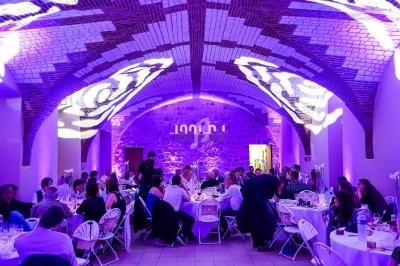 Salle voûtée en briques avec éclairage violet, tables dressées et invités assis lors d'un événement festif.