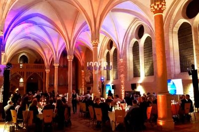 Salle voûtée éclairée avec des invités assis à des tables lors d'un événement ou d'un dîner.