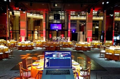 Salle de réception élégante avec tables rondes dressées et un ordinateur portable de DJ au premier plan.