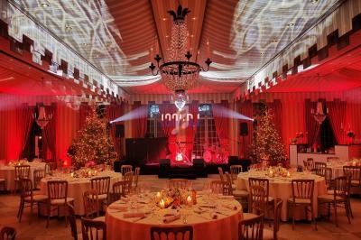 Salle de réception décorée avec des tables dressées, éclairage rouge, chandeliers et scène avec projecteurs.