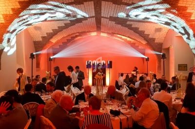 Salle voûtée éclairée en orange, avec des convives assis à des tables rondes lors d'un événement festif.