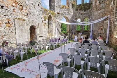 Cérémonie de mariage en plein air dans les ruines d'une ancienne église, avec des chaises blanches et une allée décorée.