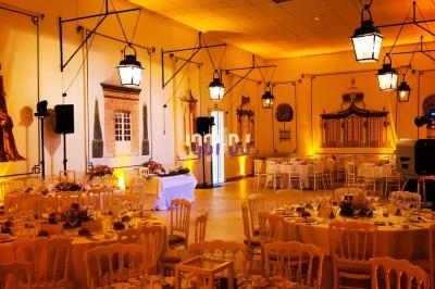 Salle de réception décorée avec des tables rondes dressées, éclairée par des lanternes suspendues et des lumières chaudes.