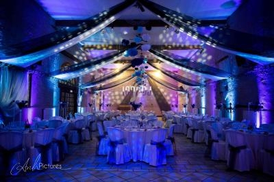 Salle de réception décorée avec des tables dressées, éclairages colorés et guirlandes suspendues au plafond.