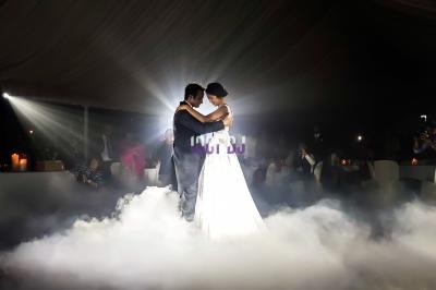 Un couple danse au milieu d'une piste entourée de fumée et éclairée par une lumière douce dans une salle sombre.