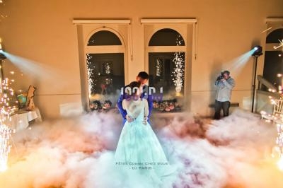 Un couple danse au milieu de fumée et d'étincelles dans une salle éclairée, sous le regard d'un photographe.