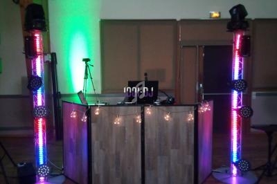 Console de DJ avec éclairage coloré et colonnes lumineuses dans une salle avec parquet et murs neutres.