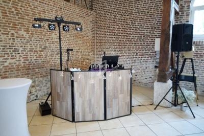 Table de DJ installée dans une salle en briques avec éclairage et équipement audio sur un sol carrelé.