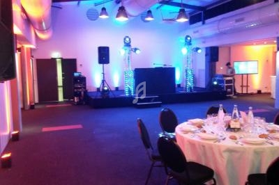 Salle de réception avec scène équipée de matériel audio et éclairage, tables dressées au premier plan.
